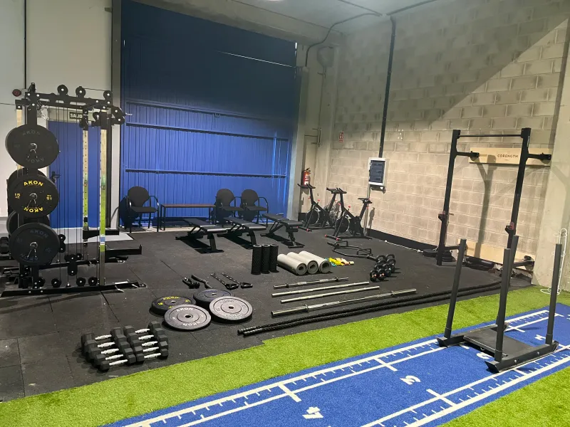 Vista general de la sala de entrenamiento con racks, discos, barras y colchonetas
